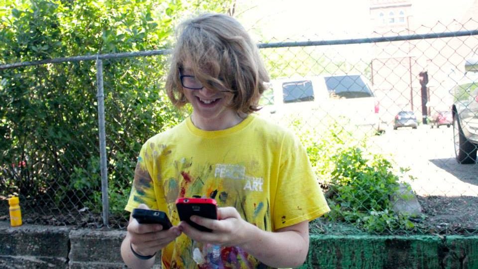 Teenager wearing yellow shirt using two smartphones